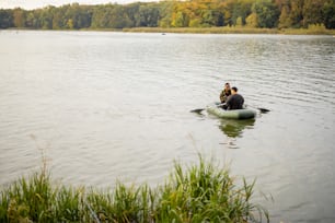 Multiracial male friends fishing with fishing rods on rubber boat in lake or river. Concept of rest and hobby in nature. Idea of friendship and spending time together. Wide view with copy space