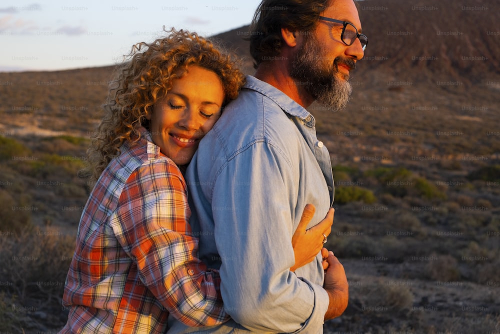 Mature young people couple in love hug and enjoy romantic activity outdoor in sunset light. Man and woman hugging and loving each other together. Mountains in background. Travel concept
