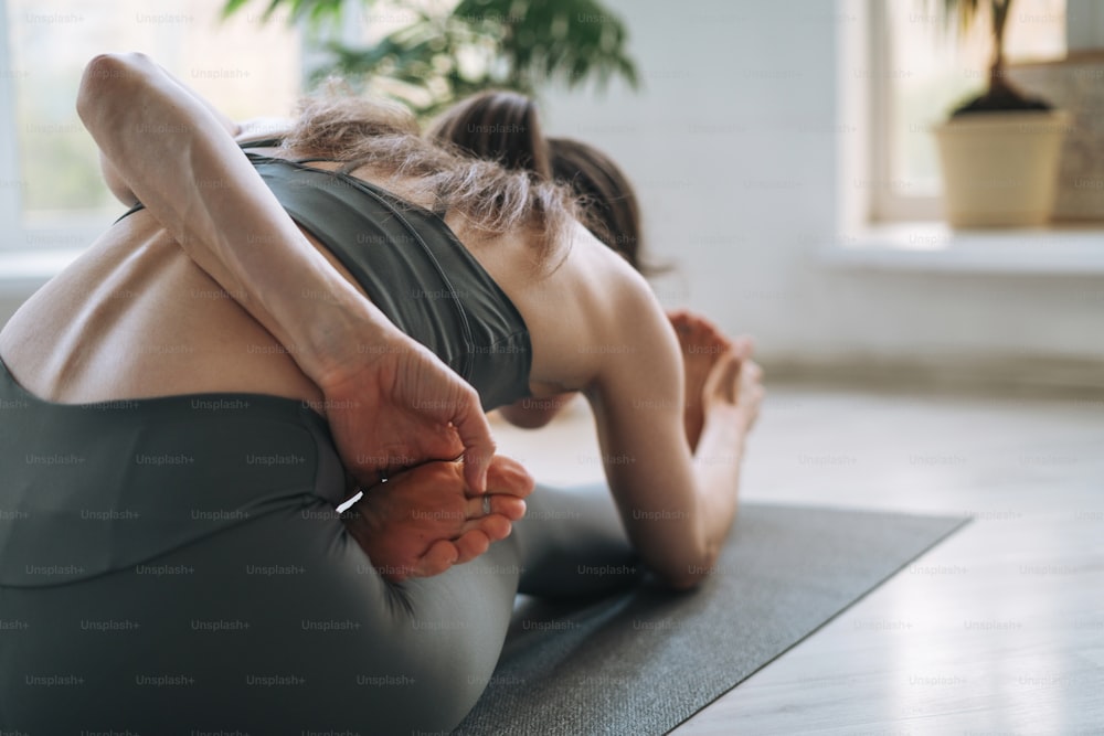 Junge fitte Frau praktiziert Yoga mit Asana im leichten Yogastudio mit grüner Zimmerpflanze