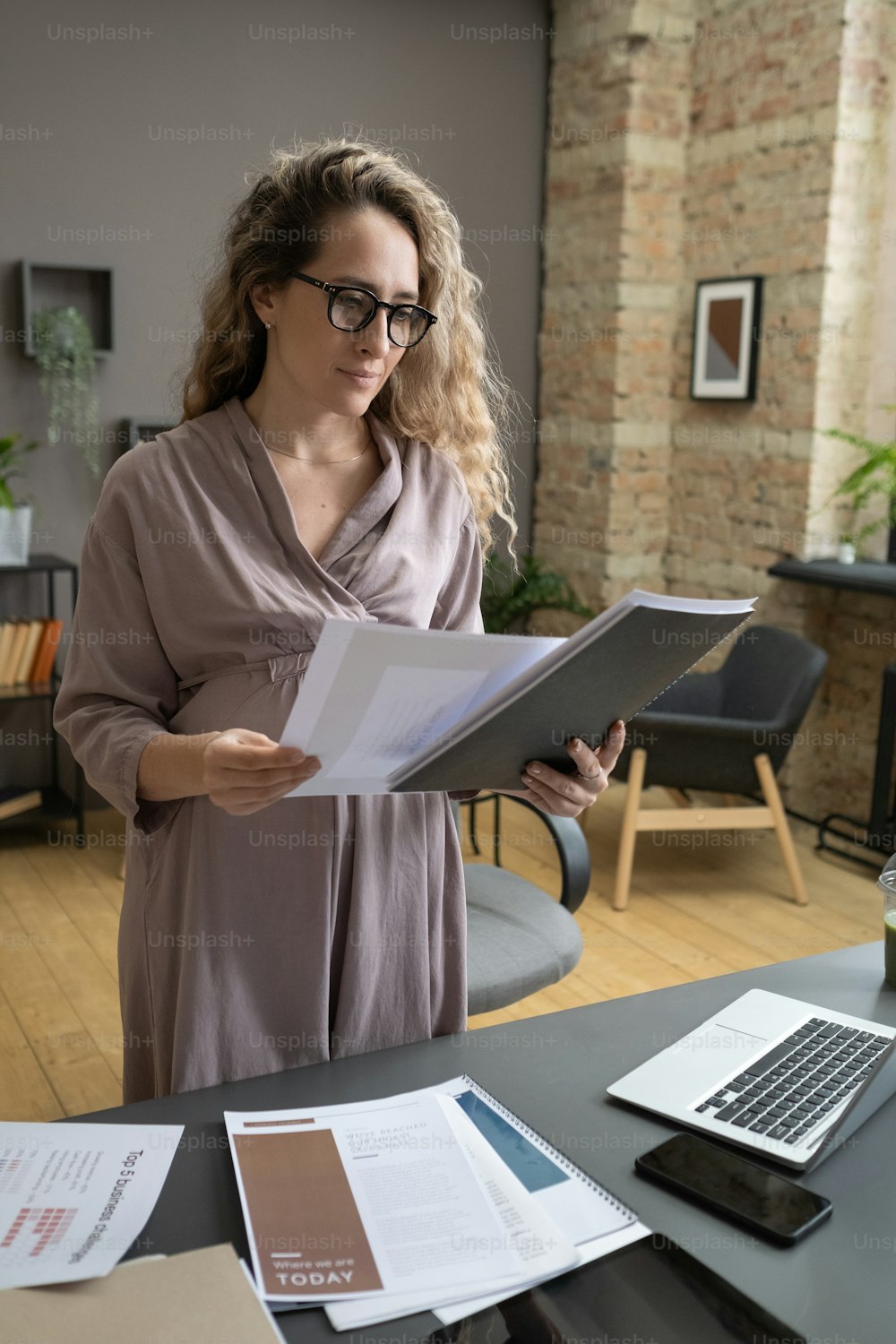 Pregnant businesswoman examining the documents in folders at the table during her work at office