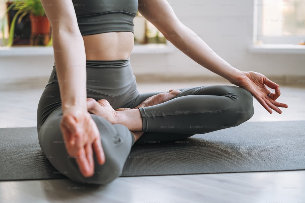 Junge fitte Frau praktiziert Yoga mit Asana-Lotus-Position im leichten Yoga-Studio mit grüner Zimmerpflanze
