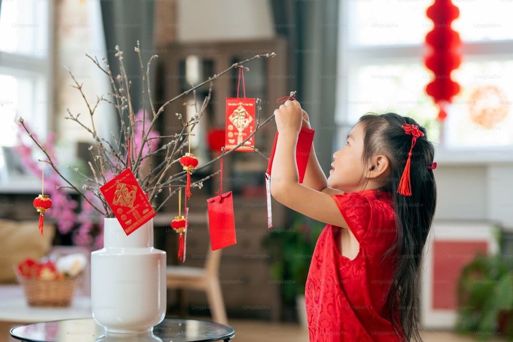 Cute little girl hanging handmade postcard containing new year greetings on branches
