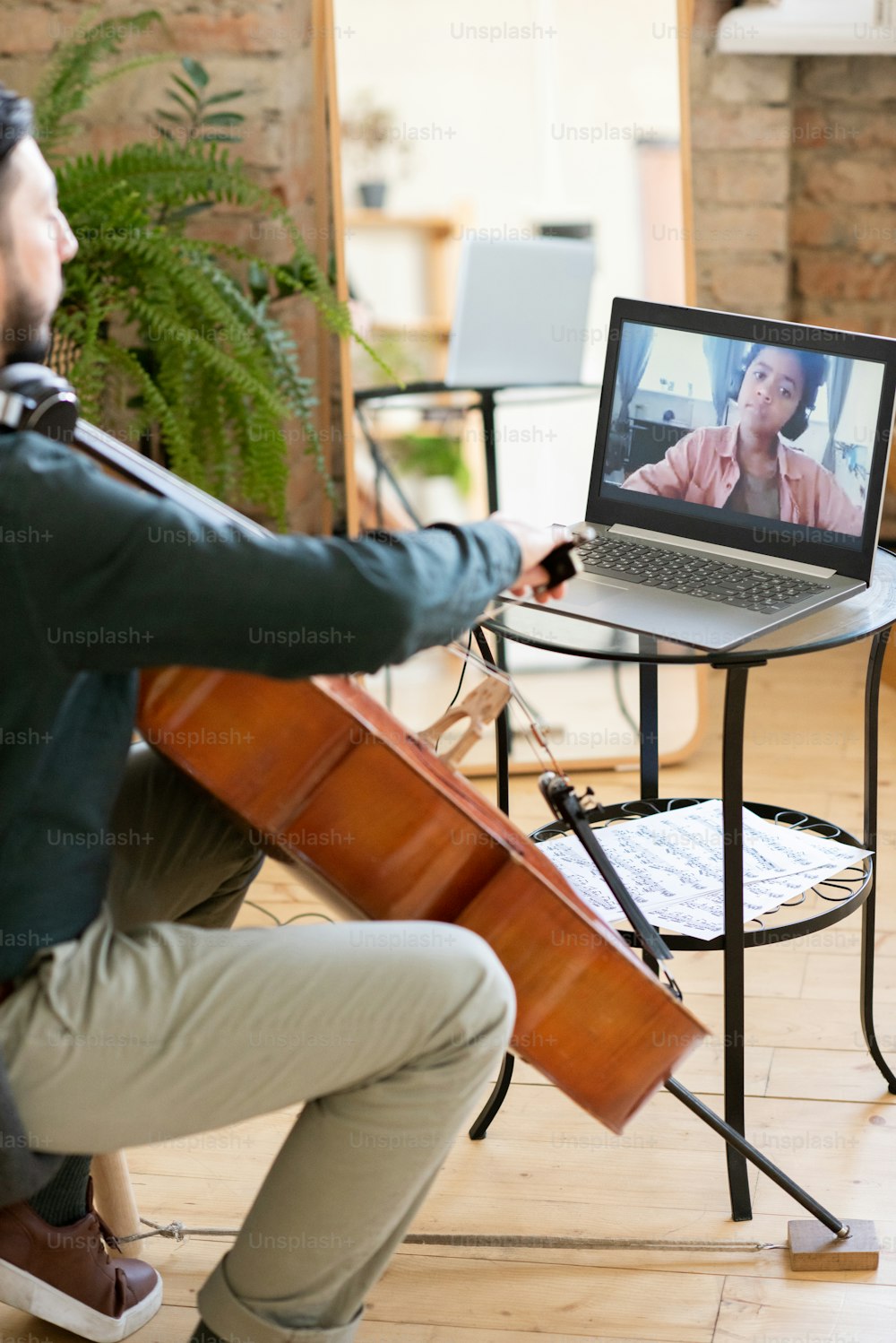 Cute African schoolboy on laptop screen looking at music teacher playing cello while sitting in home environment