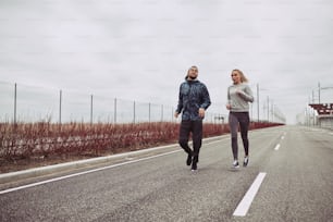 Diverse young couple in sportswear looking focused while jogging together along a road in the country