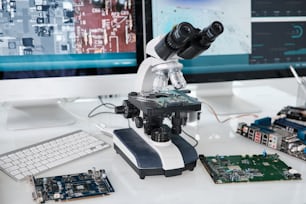 コンピュータモニター、回路基板、その他のハードウェアの間で机の上�に立つ科学研究者の顕微鏡