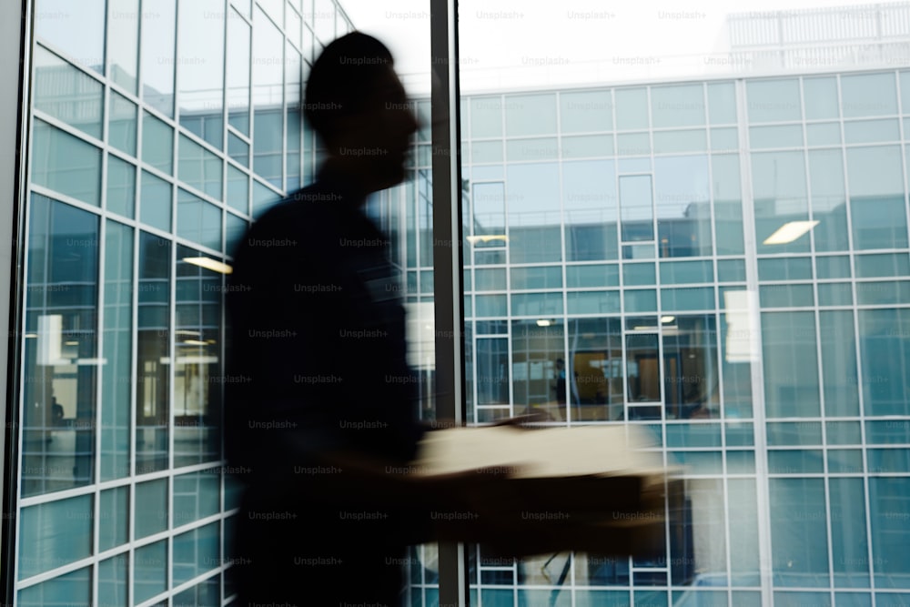 Mouvement flou d’un livreur marchant le long de la fenêtre d’un immeuble de bureaux tout en portant une pizza à l’un des clients