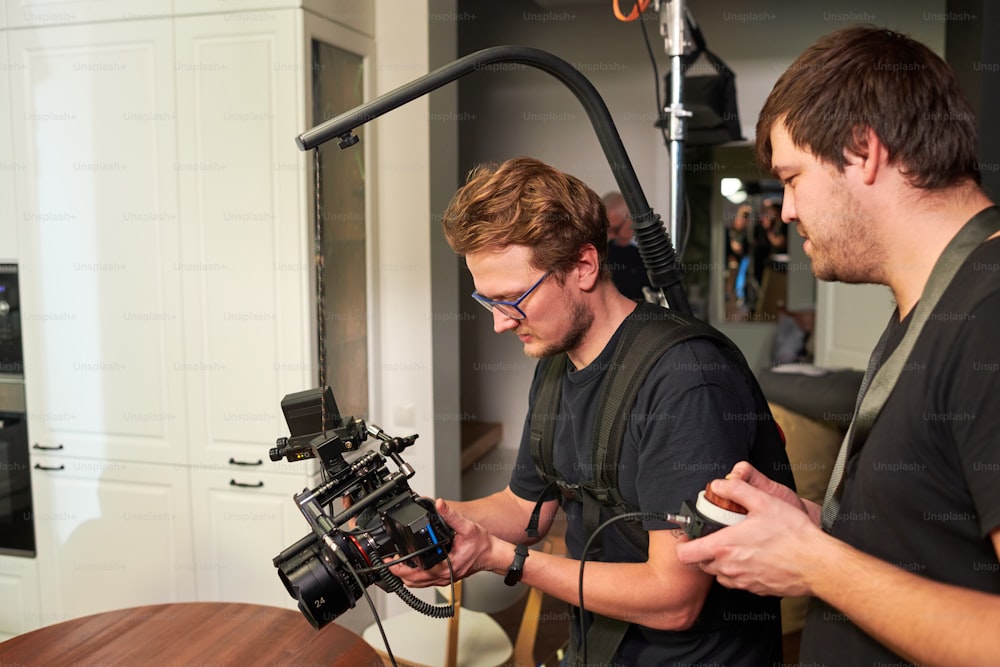 Dois cinegrafistas ou cinegrafistas e seu assistente se preparando para filmar e consultando sobre ajuste de equipamentos