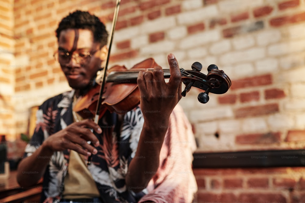 Manos de un joven negro sosteniendo un palo de violín y tocando cuerdas de violín mientras realiza una composición musical clásica
