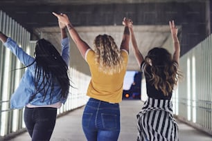 Rearview of a group of diverse young girlfriends having fun while holding hands and walking together down a walkway in the city at night