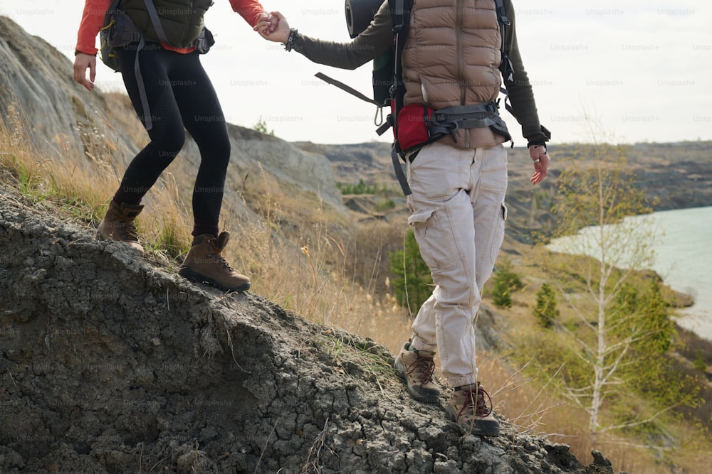Cropped shot of unrecognizable female tourists hiking around quarry lake doing down the cliff holding hands