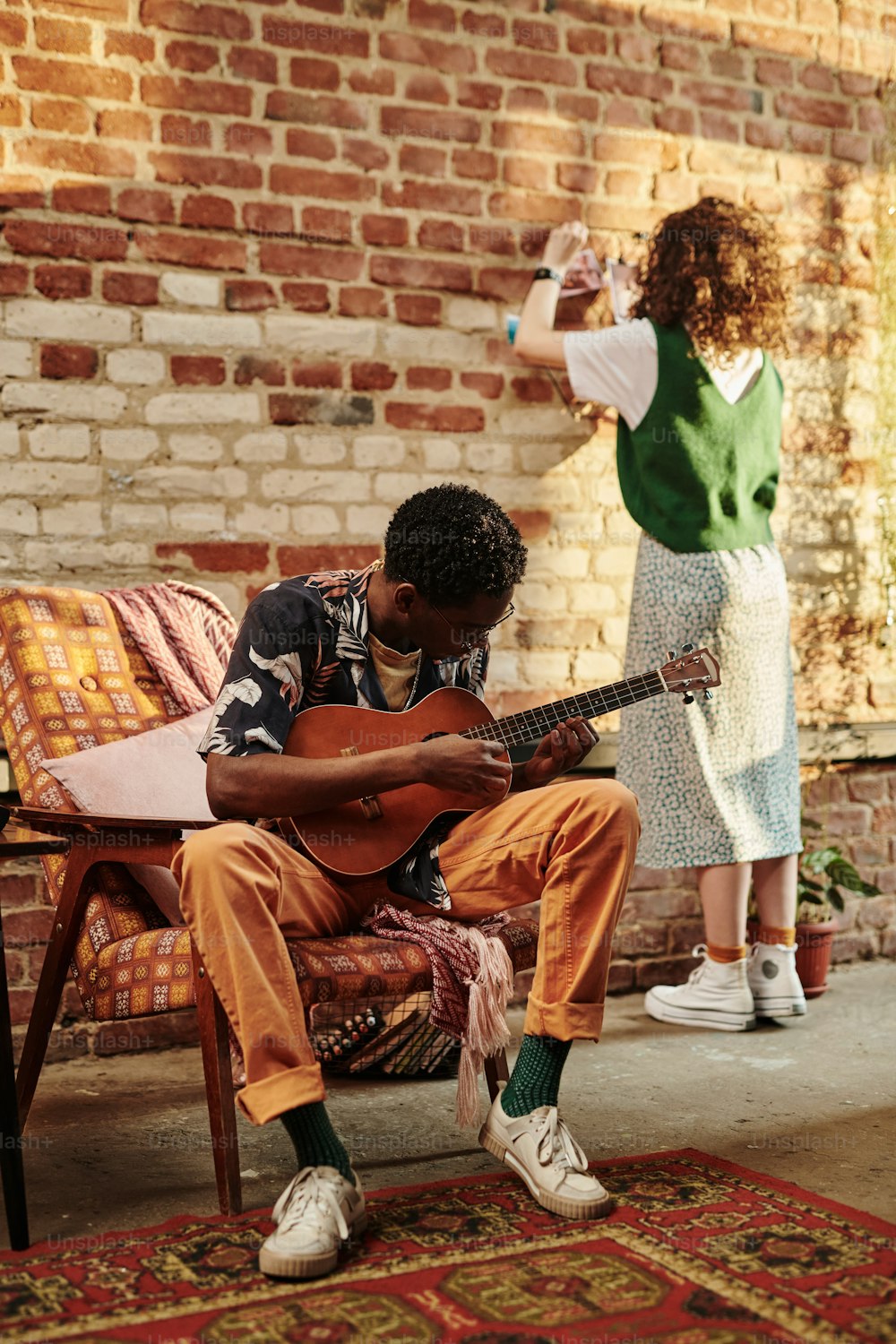 アコースティックギターを弾く若い男とガールフレンドがスタジオやモダンなロフトアパートのリビングルームのレンガの壁の前に立っている