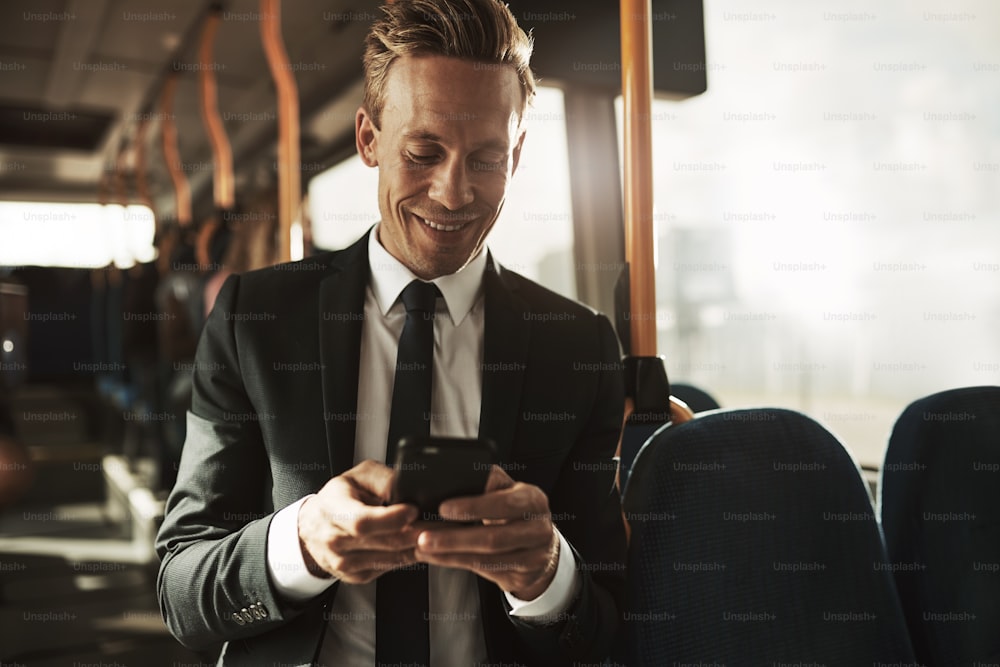 Smiling young businessman wearing a suit standing on a bus during his morning commute reading text messages