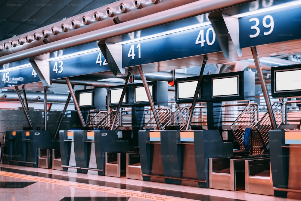 Interior del área de check-in en un aeropuerto moderno: terminales de aceptación de equipaje con sistemas de cinta transportadora de manejo de equipaje, múltiples plantillas de pantalla LCD de información blanca en blanco, mostradores de check-in indexados