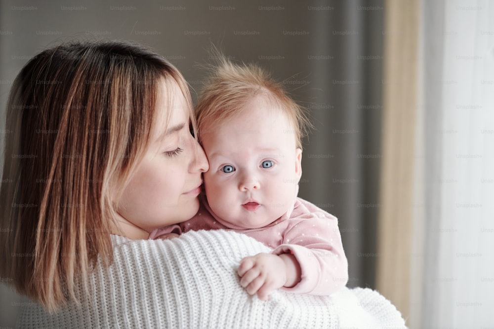 Young affectionate woman touching face of her cute baby daughter in front of camera