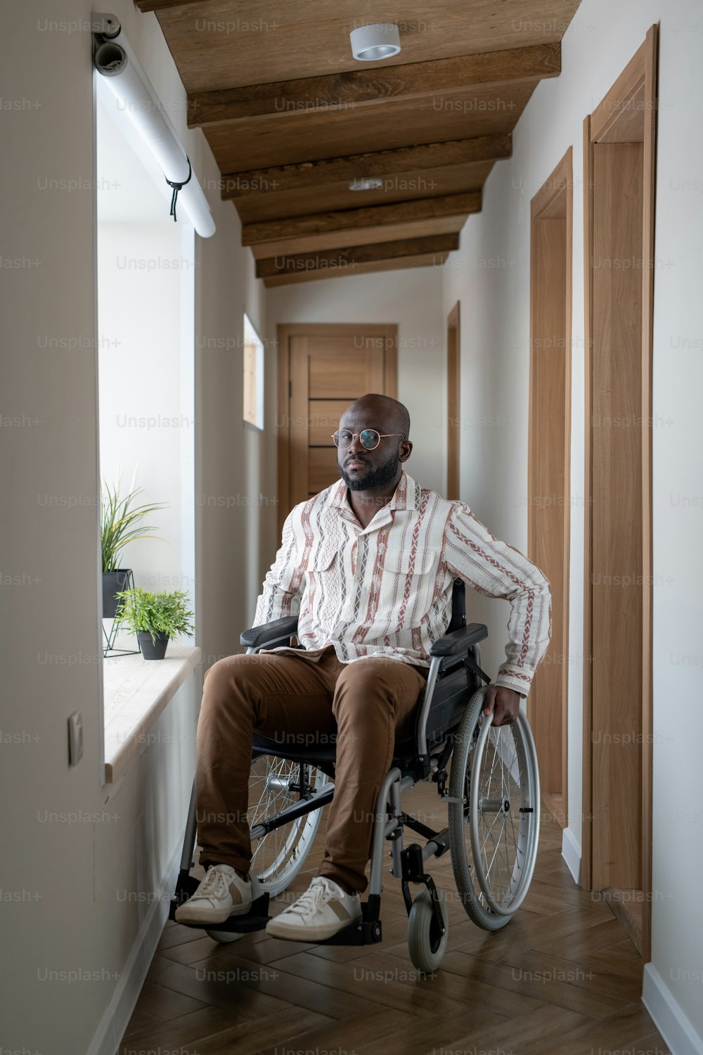 大きな近代的なアパートの長い廊下で車椅子に座り、カメラを見ている障害のあるアフリカ系アメリカ人の男性
