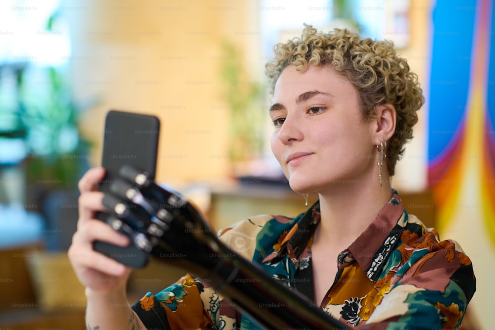 Glückliches blondes Mädchen mit myoelektrischem Arm, das Selfie macht, während es sich in einem gemütlichen Café ausruht und in die Smartphone-Kamera schaut