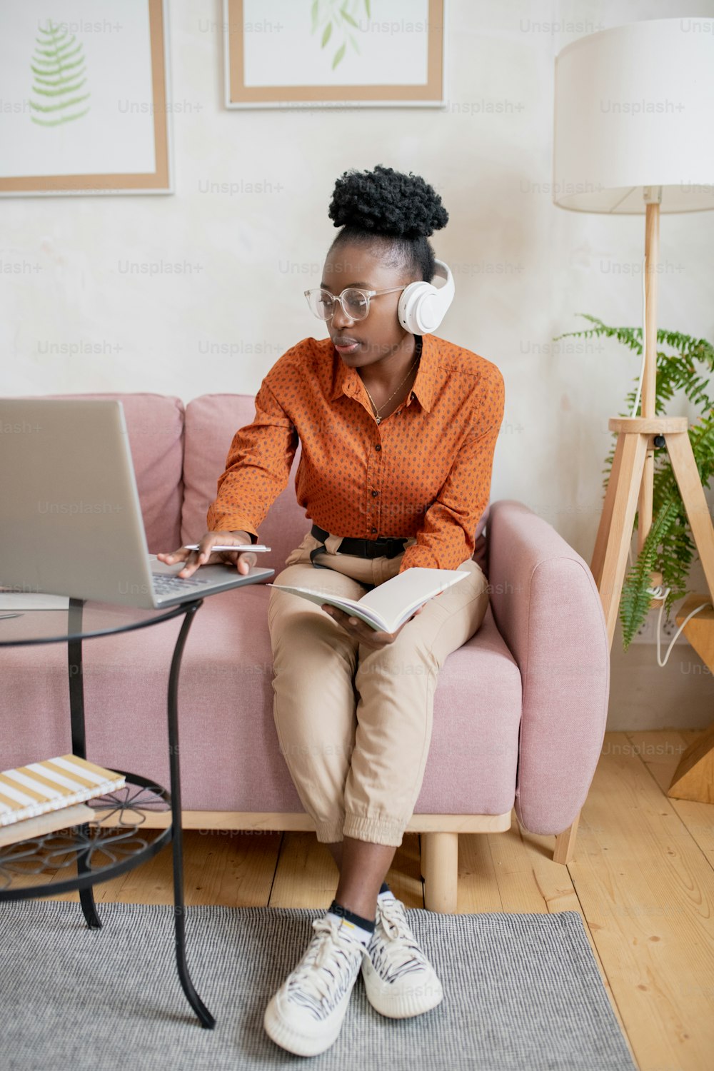 African female student in headphones looking at laptop screen while sitting on couch in home environment during online lesson