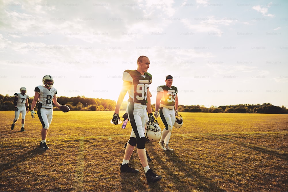 Smiling group of young American football players walking onto a grassy field together on a sunny afternoon during a football game