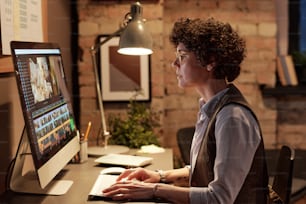 Jovem colorista profissional sentada em seu local de trabalho em frente ao monitor do computador e editando fotos em software especial