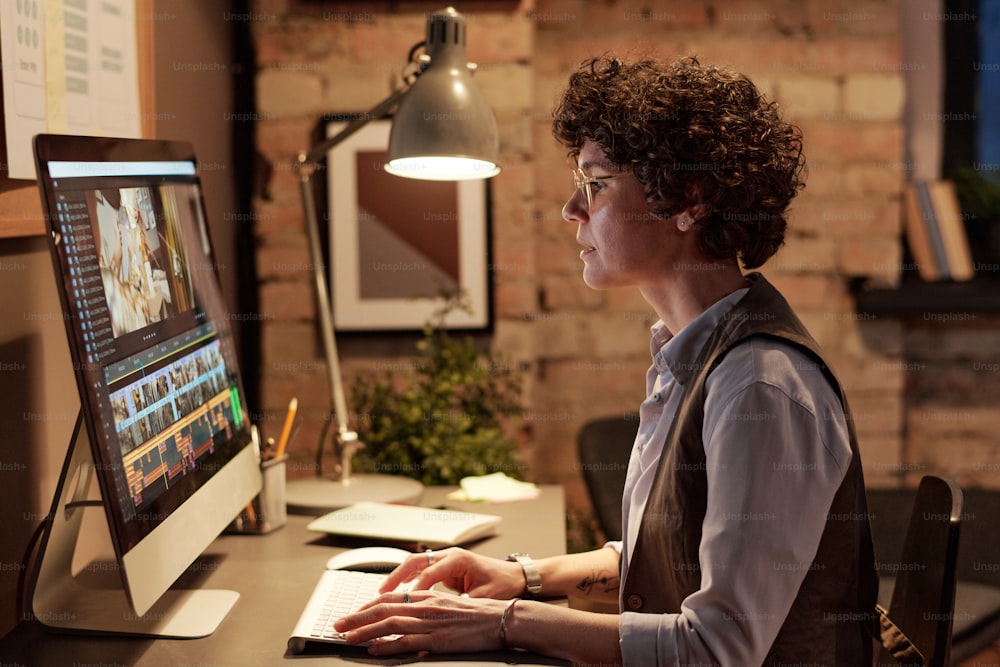 Giovane colorista professionista che si siede sul suo posto di lavoro davanti al monitor del computer e modifica le foto su un software speciale