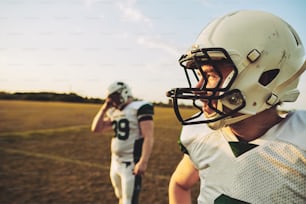 American football quarterback standing with a teammate on a grassy field on a sunny afternoon during a football game