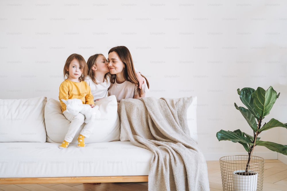 Jeune famille heureuse avec un parent femme mère avec deux enfants filles sur le canapé dans le salon à la maison