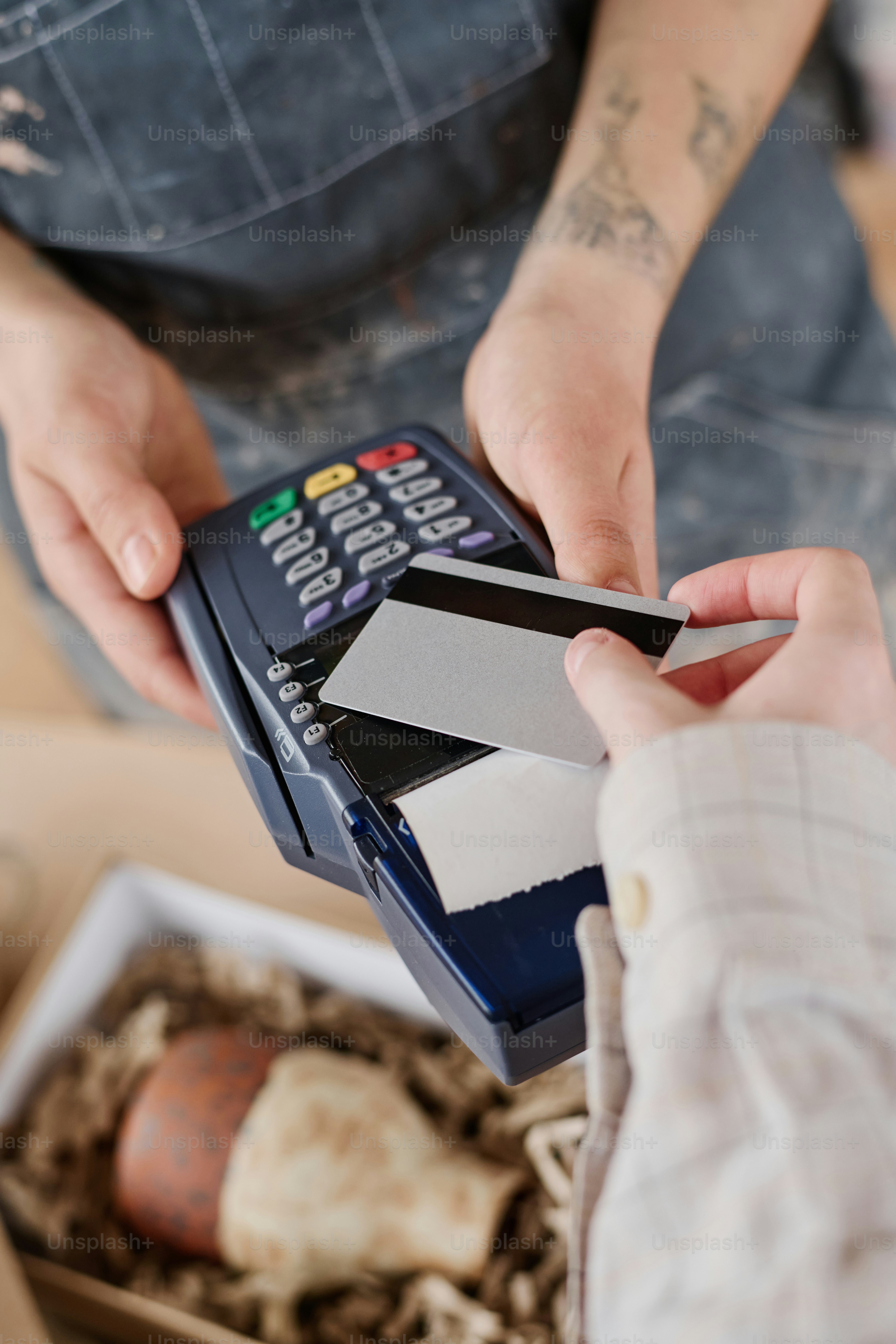 Hands of young female shop assistant with payment terminal and those of client paying for purchase of earthenware by credit card