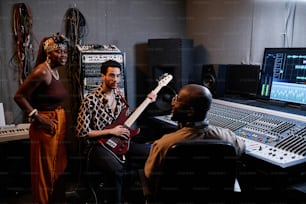 Produtor musical afro-americano maduro e dois jovens músicos discutindo algo em estúdio de gravação