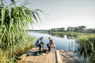 Deux pêcheurs se détendant pendant le pique-sur la belle jetée en bois avec roseau vert sur le lac le matin