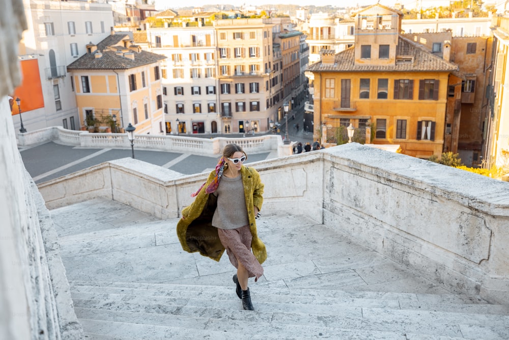Donna che corre sulla famosa scalinata di Spagna sullo sfondo della città vecchia di Roma. Donna che indossa abiti vecchio stile in stile italiano. Concetto di stile di vita italiano e visita di famosi monumenti italiani