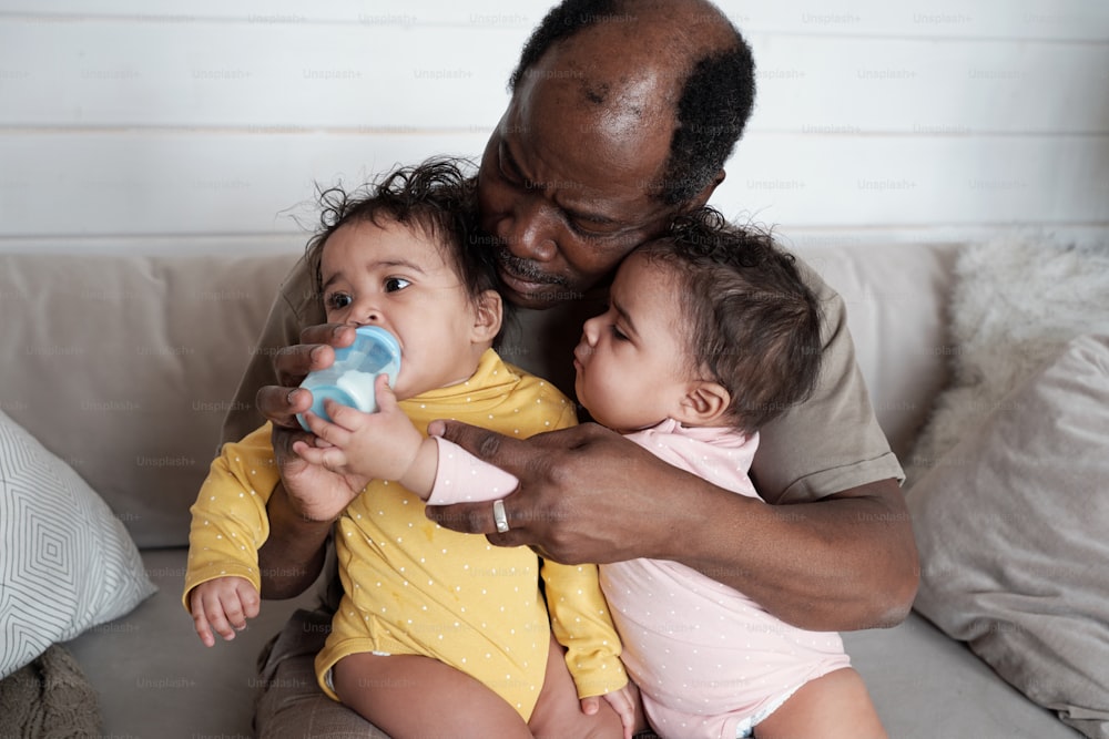 現代の成熟したアフリカ系アメリカ人の父親の肖像画は、彼の双子の赤ちゃんの哺乳瓶の世話をしています