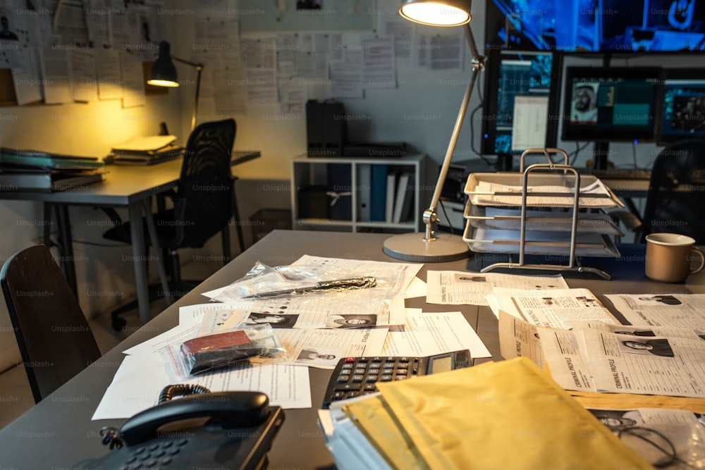 Parte do local de trabalho do agente fbi moderno com documentos, evidências, calculadora e telefone na mesa iluminado por lâmpada em pequeno escritório