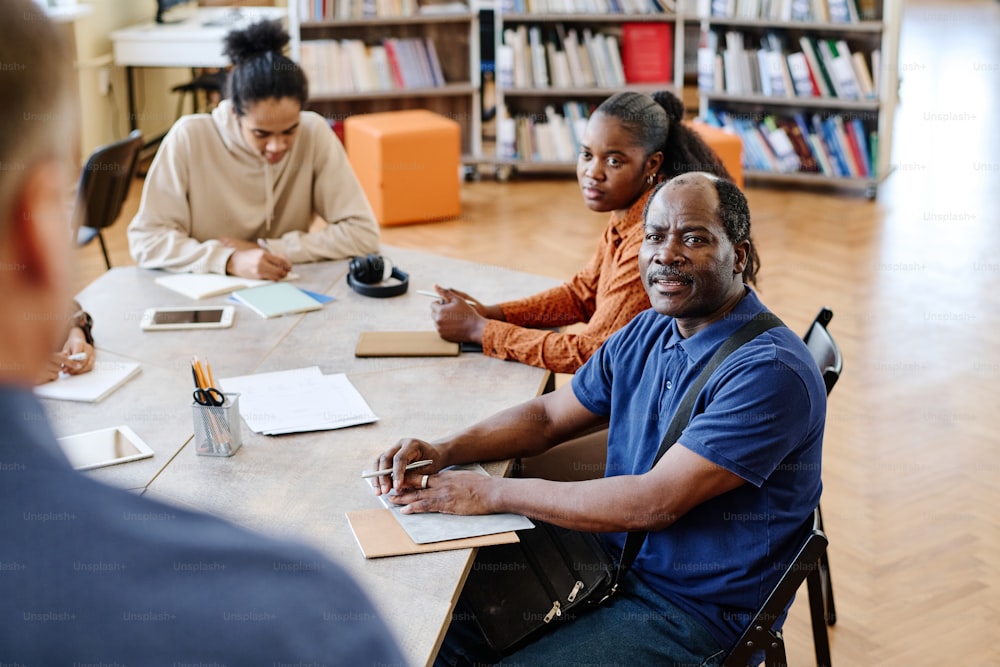 Familia moderna de migrantes negros que asisten a una clase de idiomas en una escuela internacional escuchando a un profesor