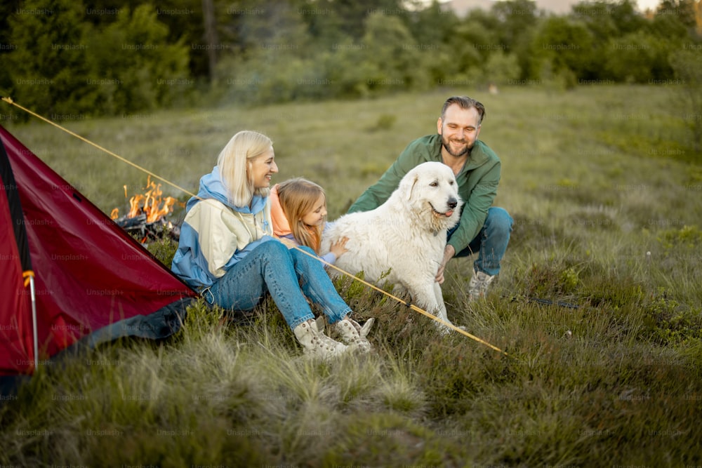 Portrait of a lovely couple with little girl and dog sit together while travel in the mountains. Young caucasian family spend summer vacation on nature