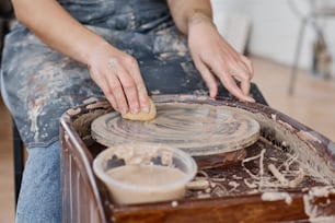 Hands of young woman wiping pottery wheel with wet sponge after creating new earthenware items for sale in workshop or studio