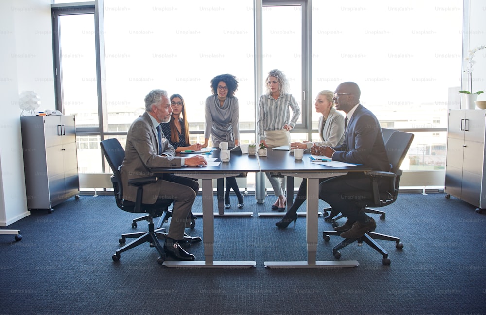 Un grupo diverso de colegas corporativos escuchando a su gerente durante una reunión de estrategia comercial en la sala de juntas de una oficina