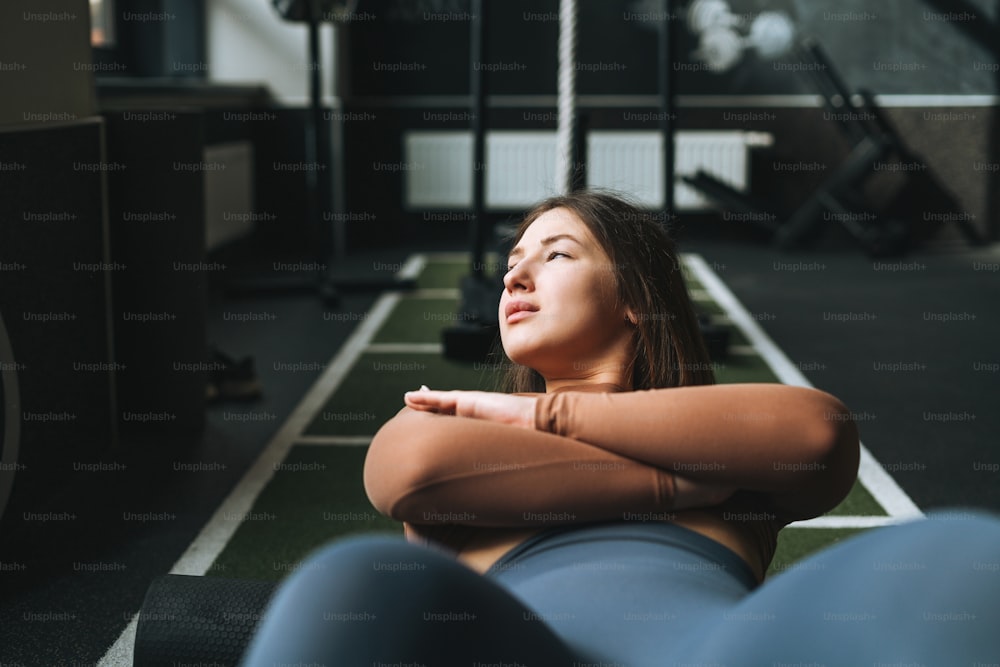 Young brunette woman doing stretching pilates, practice yoga on roller in fitness club