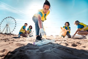 Group of eco volunteers picking up plastic trash on the beach - Activist people collecting garbage protecting the planet - Ocean pollution, environmental conservation and ecology concept