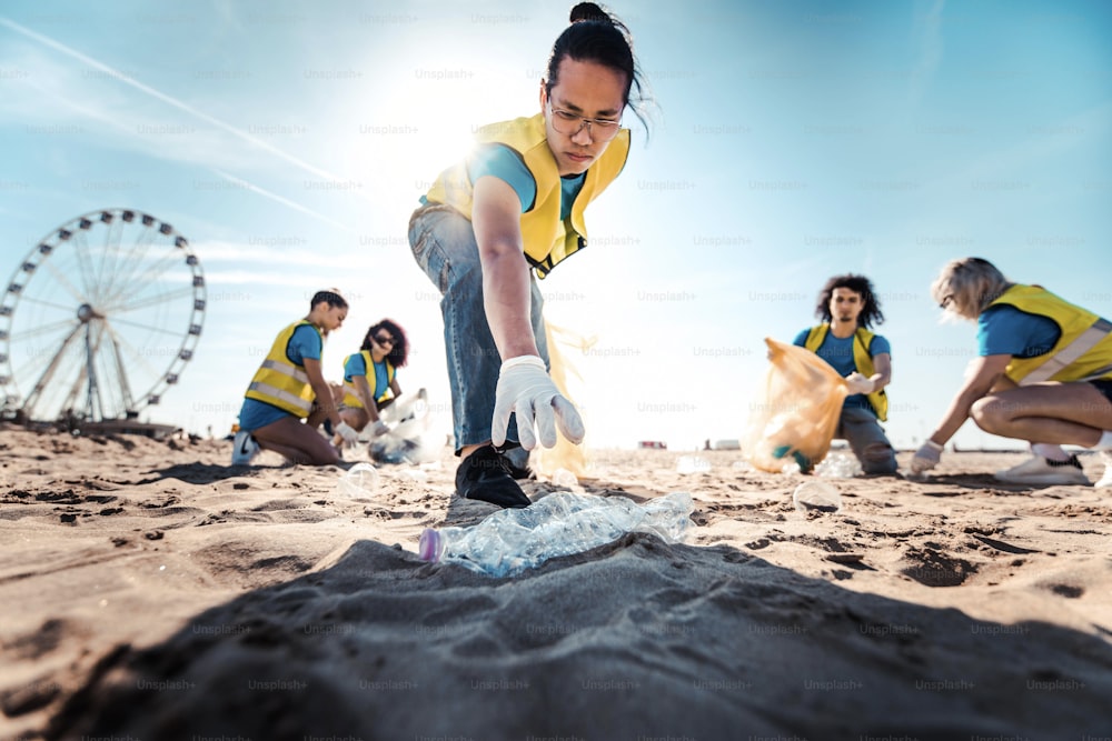 Group of eco volunteers picking up plastic trash on the beach - Activist people collecting garbage protecting the planet - Ocean pollution, environmental conservation and ecology concept