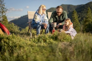 Young caucasian couple with little girl sit relaxed on chairs while traveling in the mountains. Concept of happy family vacation on nature