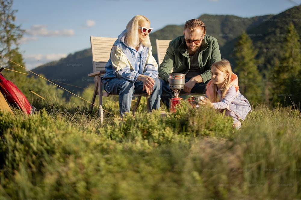 Young caucasian couple with little girl sit relaxed on chairs while traveling in the mountains. Concept of happy family vacation on nature