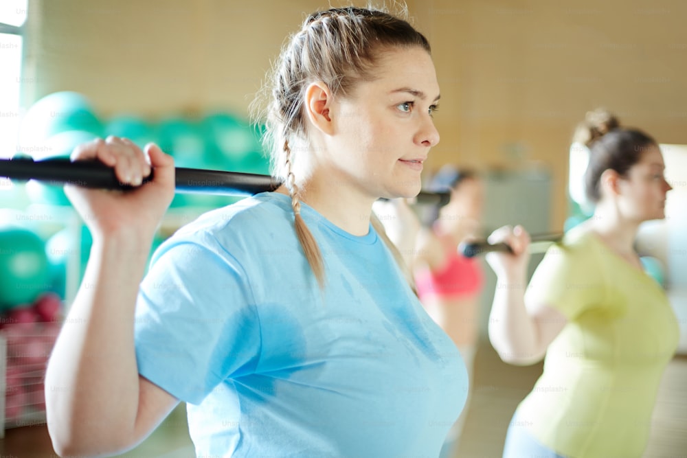 Young sweaty women with gymnastic bars doing exercises during workout