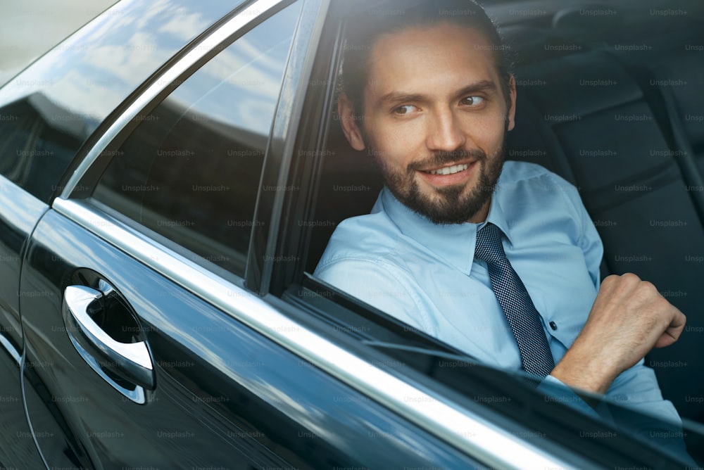 車で働くビジネスマン。フォーマルウェアを着たハンサムな成功した若いビジネスマンが車の後部座席に乗って窓から見ている肖像画。出張。高品質の画像。