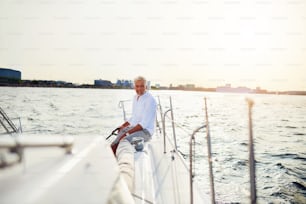 Homem maduro sentado sozinho no convés de um barco navegando ao longo da costa em um dia ensolarado