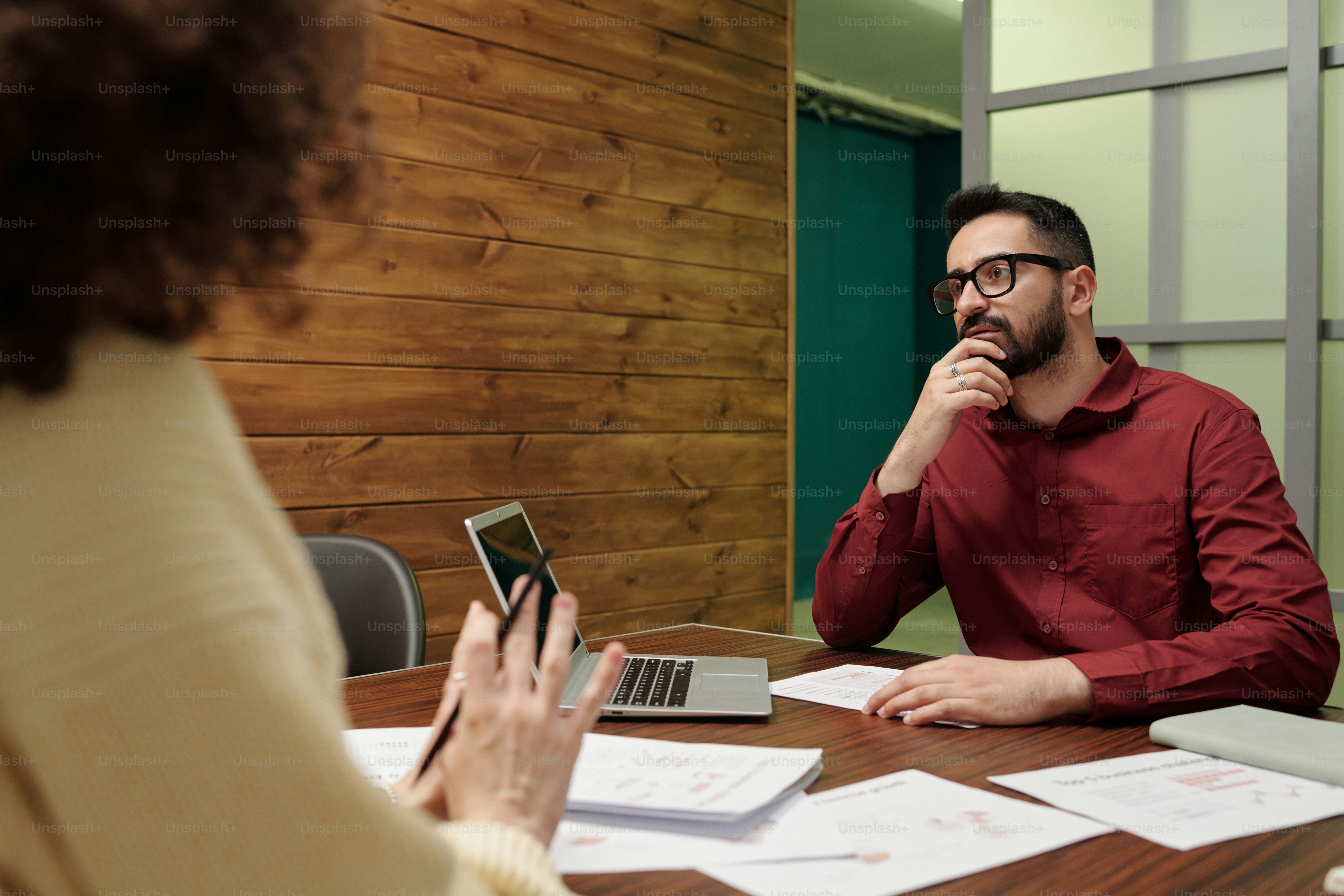 Young pensive businessman sitting in front of female colleague at working meeting or briefing by workplace in office
