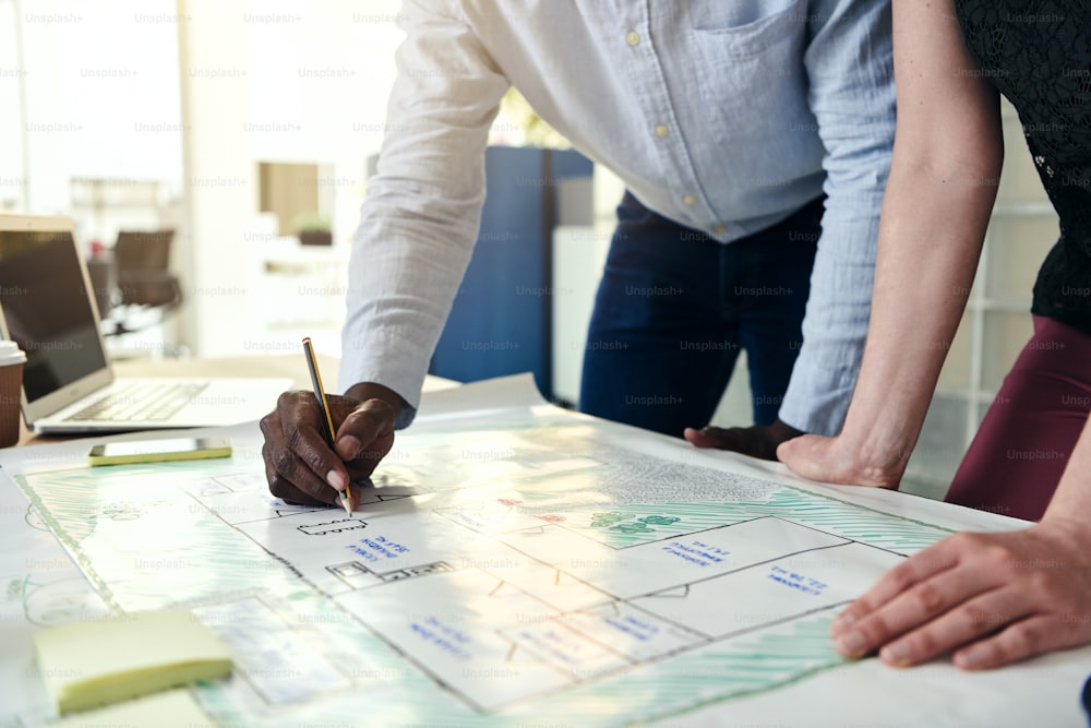 Closeup of two architects leaning over a desk discussing a building design together while standing in a modern office