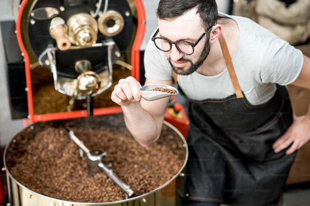 焙煎所の焙煎機のそばにスコップで立ってコーヒー豆の品質をチェックする男性
