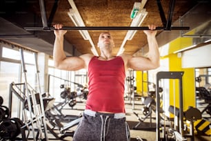 Vista frontal de perto de motivado e focado forte muscular ativo jovem careca saudável trabalhando pull-ups no ginásio moderno.