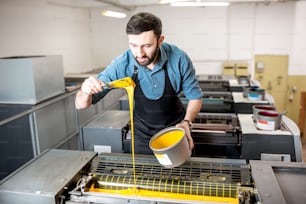 Tipografo che riempie la vernice gialla nella macchina offset alla produzione di stampa
