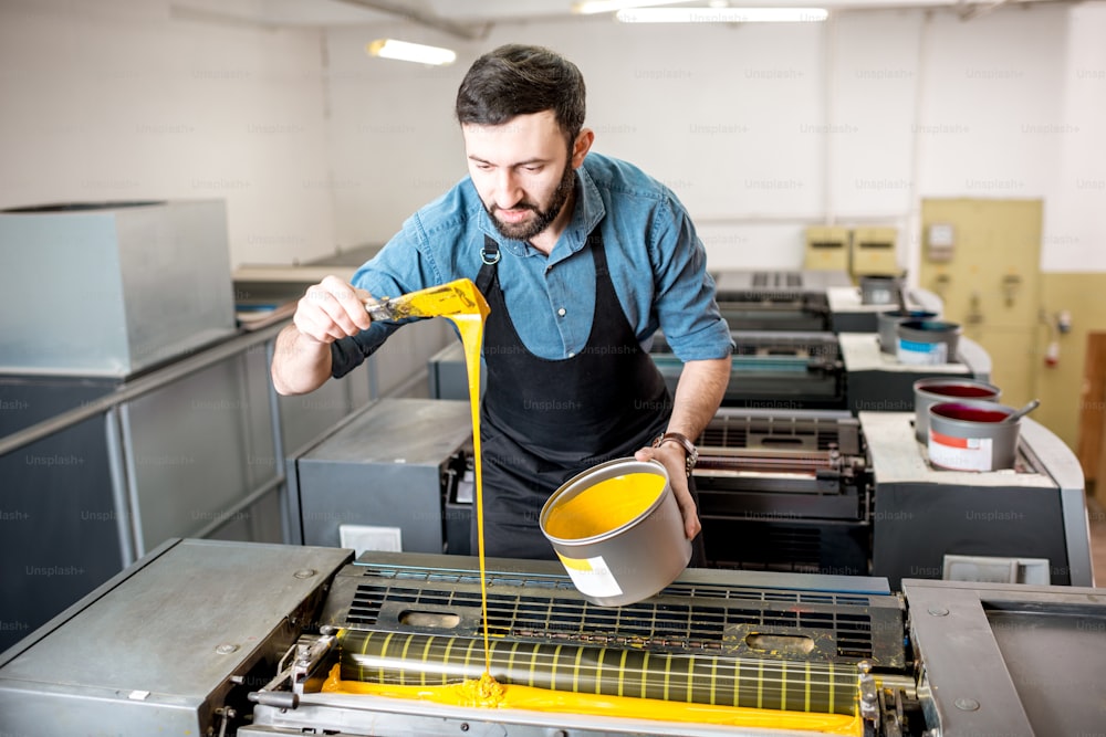 Tipógrafo enchendo tinta amarela na máquina offset na fabricação de impressão